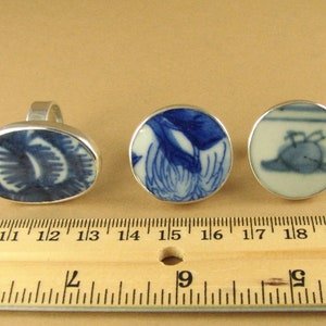 May include: Three silver rings with blue and white porcelain insets. The rings are displayed on a wooden ruler with inch markings.