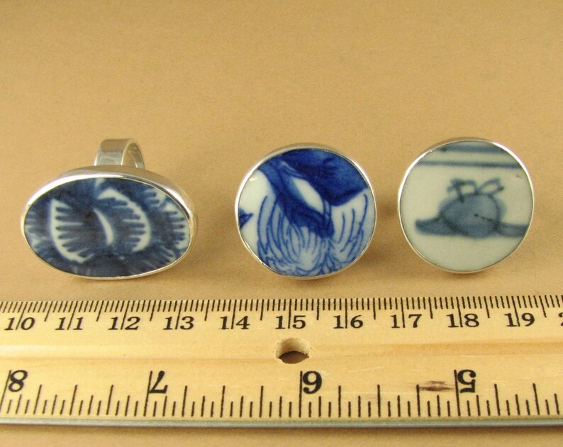 May include: Three silver rings with blue and white porcelain insets. The rings are displayed on a wooden ruler with inch markings.