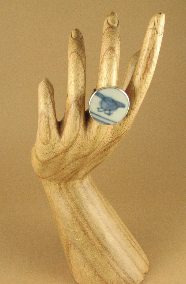 May include: A silver ring with a blue and white ceramic inlay featuring a bird design.