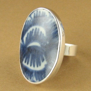 May include: A silver ring with a blue and white porcelain oval inlay. The inlay features a swirling pattern.