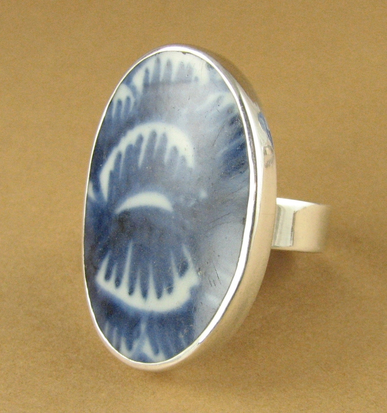 May include: A silver ring with a blue and white porcelain oval inlay. The inlay features a swirling pattern.
