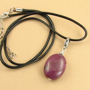 May include: A dark purple oval gemstone pendant on a black leather cord necklace. The pendant has a silver clasp and a silver wire wrap.