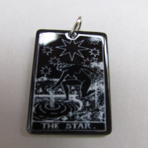 May include: Black ceramic pendant featuring a white image of a woman pouring water from a pitcher, a star, and the text "THE STAR."