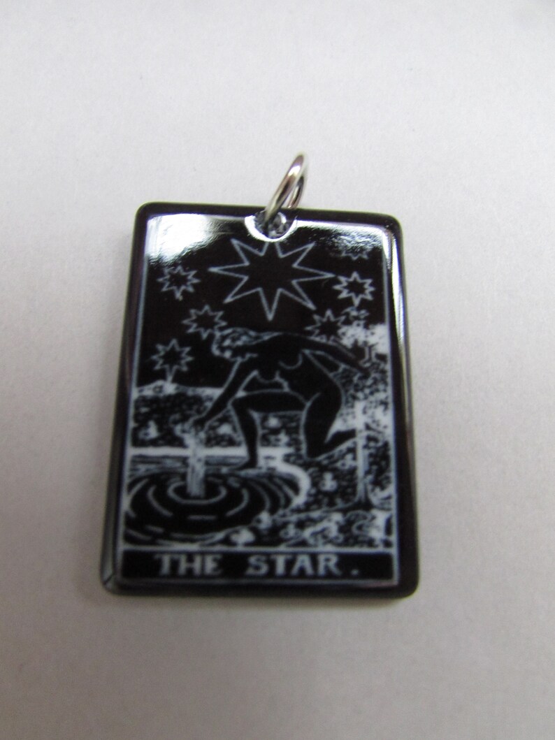 May include: Black ceramic pendant featuring a white image of a woman pouring water from a pitcher, a star, and the text "THE STAR."