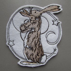 May include: Embroidered patch featuring a brown rabbit holding a smaller rabbit, surrounded by a white crescent moon and stars.