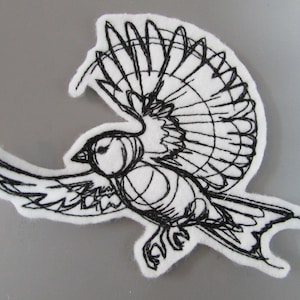 May include: Black and white embroidered patch of a bird in flight with its wings spread wide. The bird is outlined in black thread on a white felt background.