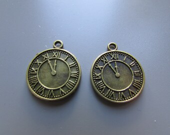 May include: Two antique gold-toned clock face charms with Roman numeral markings. The clock hands are set to 12 o'clock.