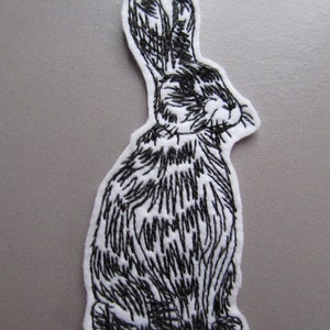 May include: Black and white embroidered patch of a rabbit sitting with its ears up.