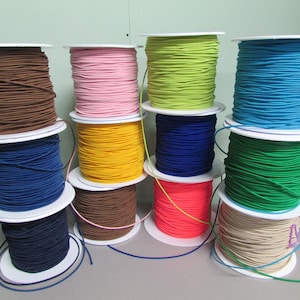 May include: Spools of colourful elastic cord in various colours including brown, pink, yellow, blue, green, and beige. The elastic cord is wound around white spools.