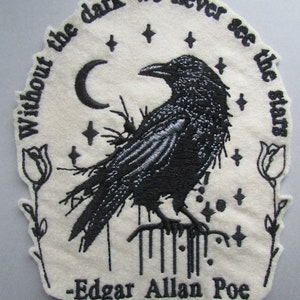 May include: An off-white fabric patch featuring black embroidery of a raven perched on a branch. The design includes a crescent moon, stars, and two roses. The text reads: Without the dark we never see the stars and -Edgar Allan Poe.