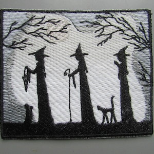 May include: Embroidered patch featuring three black silhouettes of witches with pointed hats and a black cat in front of a full moon and trees. The background is white with a silver shimmer.