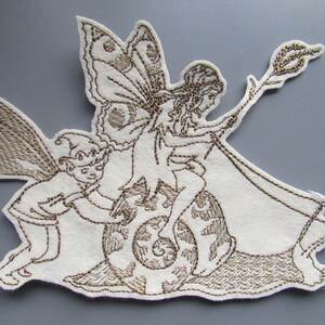 May include: Embroidered fabric applique featuring two fairies, one riding a snail and the other holding a wand. The fairies are brown and the background is white.
