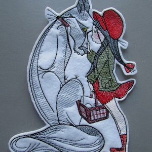 May include: Embroidered patch depicting a grey wolf and a girl wearing a red hooded dress and red boots. The wolf is looking at the girl and the girl is looking at the wolf. The girl is carrying a basket with a red and white checked pattern.
