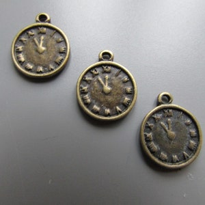 Op de afbeelding: Drie antieke goudkleurige klok-charms met Romeinse cijfers. Elke charme heeft een lus aan de bovenkant om aan een ketting of armband te bevestigen.