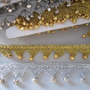 May include: Close-up of decorative trim with small bells. The trim is available in gold and silver, with a scalloped edge and dangling bells. The gold trim has a woven appearance, while the silver trim has a lace-like design.