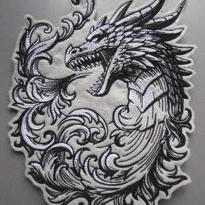 May include: Black and white embroidered patch of a dragon with its mouth open, surrounded by ornate floral designs.