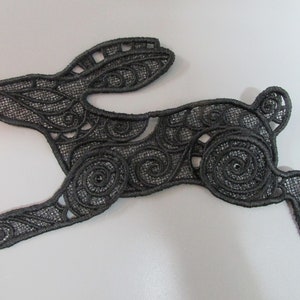 May include: Black lace applique of a stylised rabbit with intricate swirling patterns.