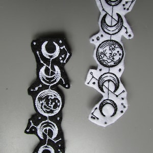 May include: Two embroidered patches depicting the phases of the moon. One patch is black with white embroidery, the other is white with black embroidery.