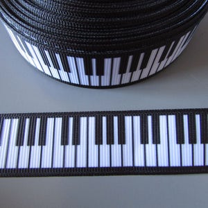 Peut inclure: Ruban noir et blanc à motif de touches de piano. Le ruban est enroulé et une section est posée à plat pour montrer le motif.