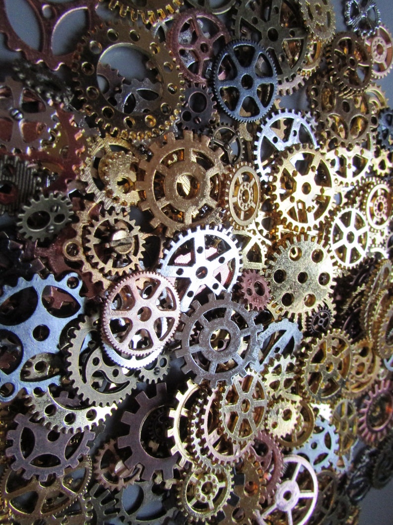 May include: A collection of various sized metal gears in shades of gold, bronze, silver, and copper. The gears are arranged closely together, creating a textured, industrial aesthetic. The image showcases the intricate details and mechanical design of the gears.
