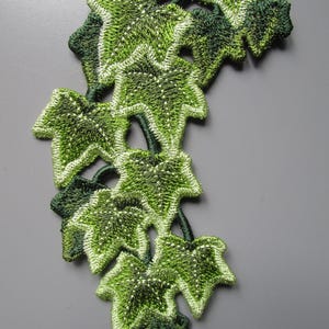 Könnte beinhalten: Ein gestickter Aufnäher mit einer Ansammlung von Efeublättern in verschiedenen Grüntönen, die von hellem Limettengrün bis zu tiefem Waldgrün reichen. Das Design zeigt detaillierte Stickereien, die die Blattadern und Ränder in einem Rankenmuster definieren.