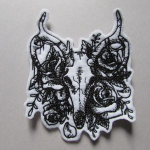 May include: Black and white embroidered patch featuring a skull with antlers surrounded by roses and foliage.