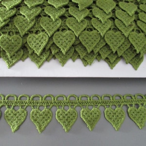 Può includere: Primo piano di un bordo in pizzo verde a forma di cuore. Il bordo è di una tonalità verde vibrante e presenta un motivo ripetuto di forme a cuore. Il pizzo viene probabilmente utilizzato per abbellire abiti o progetti artigianali.