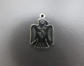 May include: A silver charm in the shape of an eagle with intricate details. The eagle is facing forward with its wings spread out.