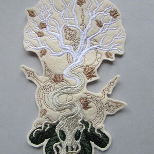 May include: Embroidered patch featuring a white tree with gold leaves, its roots forming a skull with green accents. The tree is surrounded by a circular design.