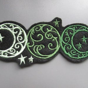 以下が含まれることがあります： 三日月と星が刺繍されたパッチ。三日月は白で縁取られ、緑色の渦巻き模様が施されています。背景は黒です。