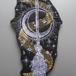 May include: A black felt patch with a white and gold embroidered design of a crescent moon, a shooting star, and a wand. The design is surrounded by small white stars.