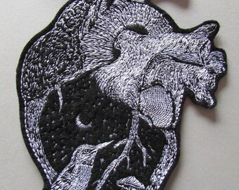 May include: Embroidered patch in the shape of a human heart, featuring a detailed black and white design. The interior depicts a night scene with a bird, mushrooms, and a crescent moon. The patch has a black border.