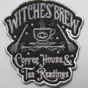 Könnte beinhalten: Ein schwarzer gestickter Aufnäher mit silbernem Faden, der eine dampfende Tasse Kaffee mit einer Sichelmond und Sternen darstellt. Der Text lautet "Witches Brew Coffee House & Tea Readings".