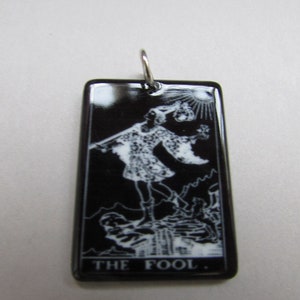 May include: Black and white tarot card pendant featuring The Fool card. The pendant is made of black enamel with a silver bail.