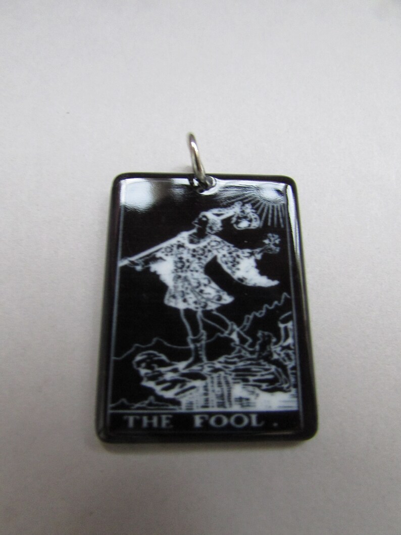 May include: Black and white tarot card pendant featuring The Fool card. The pendant is made of black enamel with a silver bail.