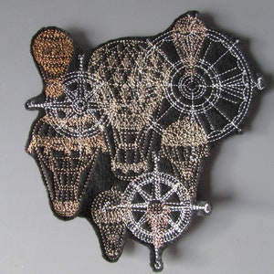 May include: Embroidered patch with a black background and gold and silver thread. The patch features four hot air balloons with a compass and a wheel design.