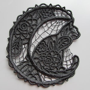 May include: Black lace applique featuring a crescent moon and a cat design. The design is intricate and detailed, with floral motifs throughout.