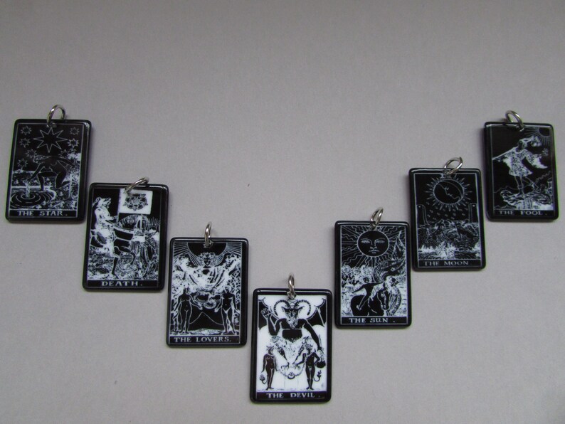 May include: Black and white tarot card charms with silver rings. The cards include The Star, Death, The Lovers, The Devil, The Sun, The Moon, and The Fool.