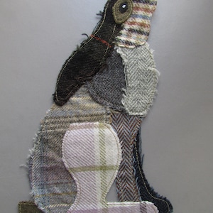 Könnte beinhalten: Eine Patchwork-Stoffhasenskulptur mit schwarzem Kopf, braunem und weißem kariertem Körper und rosa und grünem kariertem Beinen. Der Hase sitzt mit dem Kopf nach hinten geneigt.