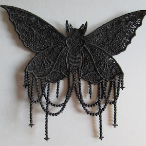 May include: A black lace butterfly applique with intricate wing details and beaded fringe. The butterfly has a detailed design and is suitable for various craft projects. The applique is approximately 10 inches wide.