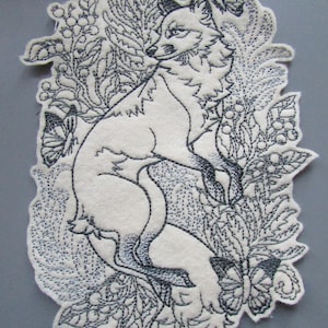 May include: An embroidered patch featuring a black and white fox standing on its hind legs surrounded by black and white floral designs and butterflies.