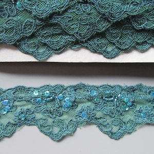 May include: Teal lace trim with sequins. The lace has a scalloped edge and a floral design.