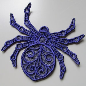 May include: A dark purple embroidered spider applique with detailed open-weave design. The spider features eight legs and a detailed body, ideal for adding a spooky touch to clothing or crafts. The applique is made of a delicate fabric.