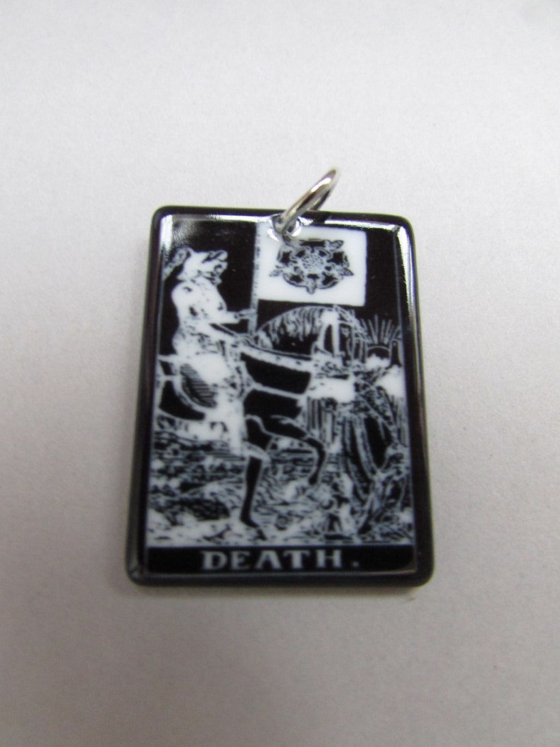 May include: Black and white ceramic pendant featuring a tarot card image of Death, a skeletal figure riding a white horse. The pendant has a silver bail and the word "DEATH" is printed in white at the bottom.