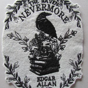 May include: An embroidered patch with a black raven perched atop a stack of books and roses. The text "THE RAVEN NEVERMORE EDGAR ALLAN POE" is embroidered in black on a white oval background, framed by black leaves.
