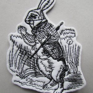 May include: Black and white embroidered patch of the White Rabbit from Alice in Wonderland. The rabbit is wearing a waistcoat and holding a pocket watch and a walking stick.