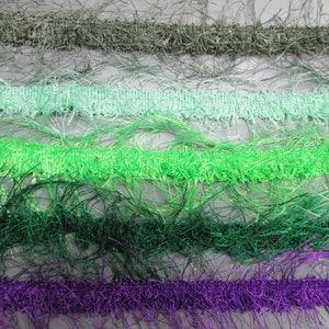 May include: Five different types of fringe trim in various shades of green and purple. The fringe is made of a soft, fluffy material and is perfect for adding a touch of texture and whimsy to any project.