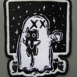 Könnte beinhalten: Gestickter Aufnäher mit einer schwarzen Katze in einem weißen Geisterkostüm, die eine Tasse hält. Der Geist hat ein X auf jedem Auge und ist vor einem schwarzen Sternenhimmel platziert. Der Aufnäher hat einen schwarzen Rand mit weißen Nähten.