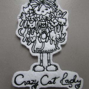 May include: Black and white embroidered patch of a woman with a lot of cats on her. The text "Crazy Cat Lady" is below the woman.