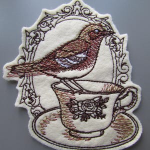 Parche bordado para coser con diseño de pájaro en una taza de té.